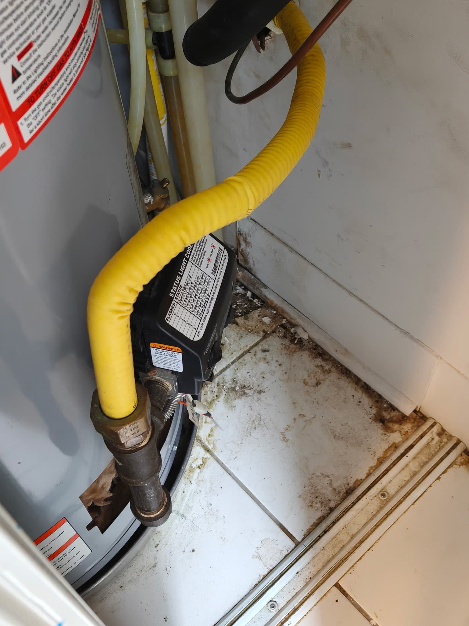 Utility room beside a water heater before cleaning, with dirt and debris on the tiled floor.